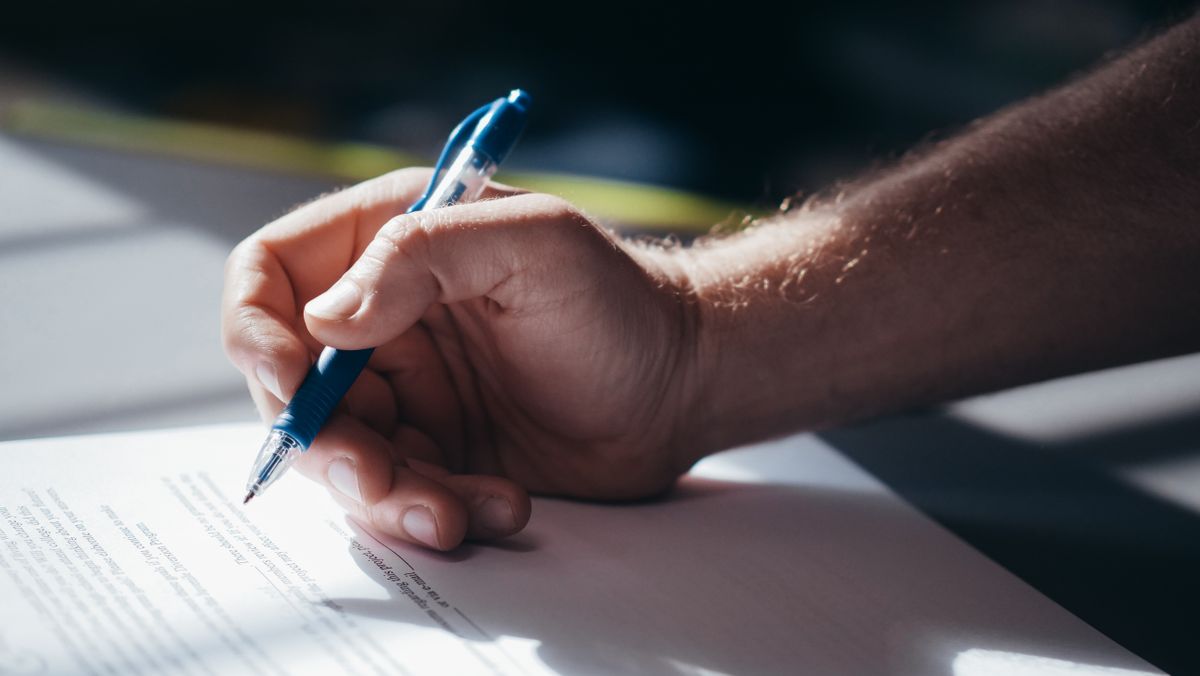 Mão assinando contrato com caneta em documento legal